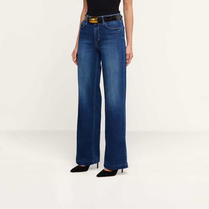 A person wearing the Scottie Wide-Leg Jean with a contoured waistband, paired with a black belt featuring a gold buckle, a black sleeveless top, and black pointed-toe heels stands against a plain white background.