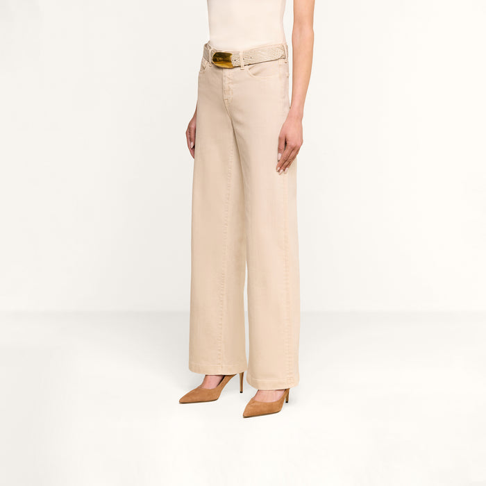 A person wearing the Scottie Wide-Leg Jean in beige—crafted from premium stretch denim and featuring a high-rise, wide-leg silhouette—is styled with a matching beige belt and tan pointed-toe heels, standing against a plain white background. The upper body and head are not visible.