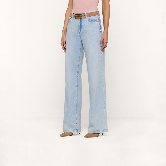 A person wearing the Scottie Wide-Leg Jean in a light wash, styled with a brown belt, a pink top, and beige pointed-toe heels stands against a plain white background.
