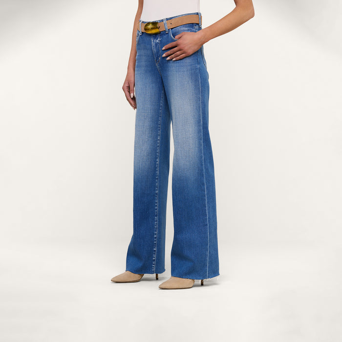 Wearing the Scottie Wide-Leg Jean with a high waist and raw hem, styled with a light brown belt and beige pointed-toe shoes, standing against a plain white background. Upper body is partially out of frame.