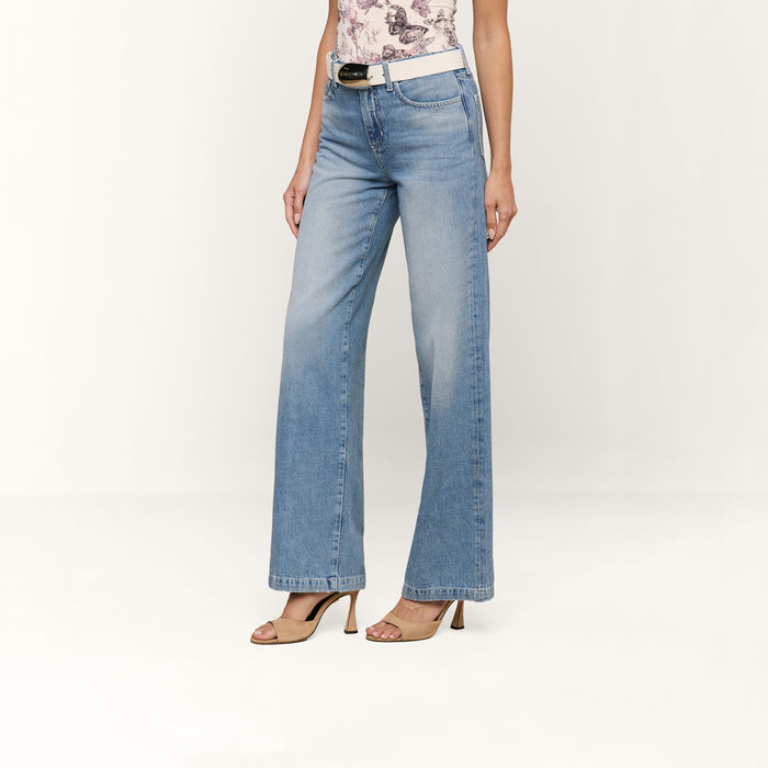 A person wears the Scottie Wide-Leg Jean in light blue all-cotton denim, styled with a white belt, sleeveless floral top, and beige heeled sandals, standing against a plain white background.