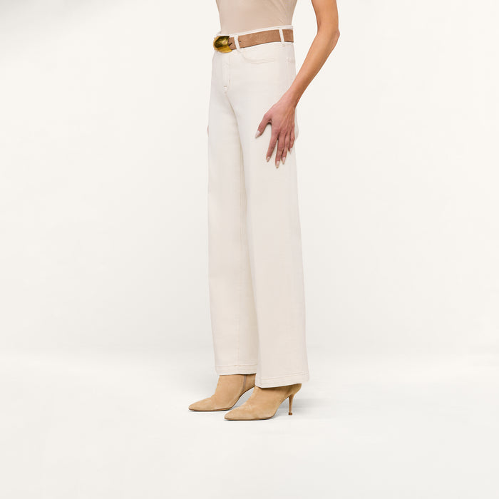 A person wearing the Scottie Wide-Leg Jean in cream, styled with a brown belt and beige heeled shoes, stands against a plain white background.