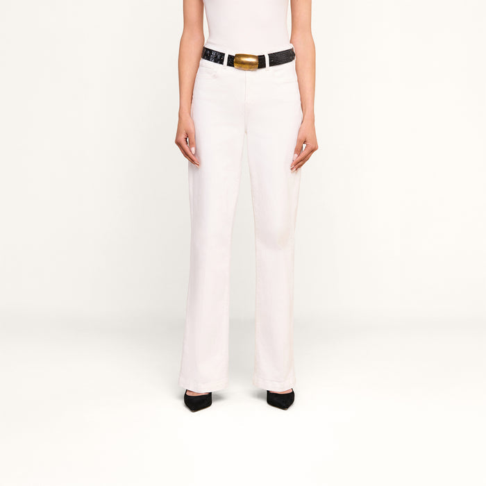 Model wearing the Scottie Wide-Leg Jean, featuring a high-rise waistband, styled with a black belt with a large gold buckle, black heels, and a white sleeveless top. The image is shot against a plain white background with the head and upper arms cropped out.
