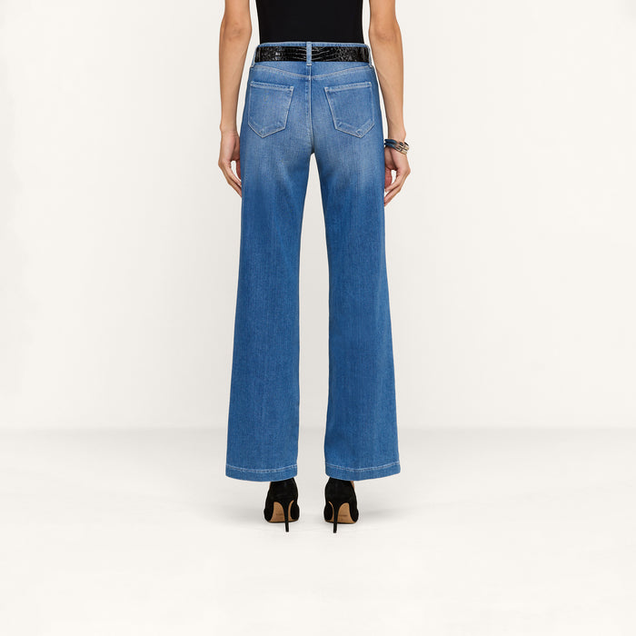 A person stands with their back to the camera, wearing the Scottie Wide-Leg Jean made of stretch denim, paired with a black belt, black top, and black heels against a plain white background.