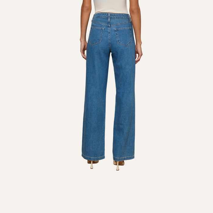 A person is shown from the back, standing against a plain white background, wearing the Scottie Wide-Leg Jean crafted from all-cotton denim in a medium wash and paired with beige heels.