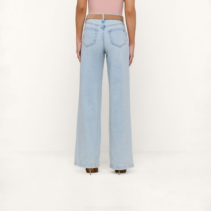 A person stands facing away against a plain white background, showcasing the back of the Scottie Wide-Leg Jean in a high-rise, light wash style, paired with a pink top.