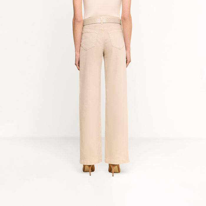 A person stands facing away, wearing the Scottie Wide-Leg Jean in a light beige wash with back pockets and tan high-heeled shoes against a plain white background.