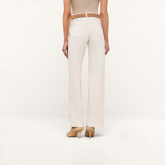 A woman stands facing away against a plain white background, wearing the Scottie Wide-Leg Jean in a cream color, paired with a beige sleeveless top and beige heeled shoes.