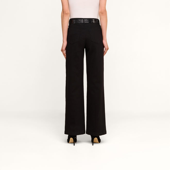 A person stands facing away on a plain white background, wearing a white sleeveless top, the Scottie Wide-Leg Jean in black high-rise, a black belt, and black heels.