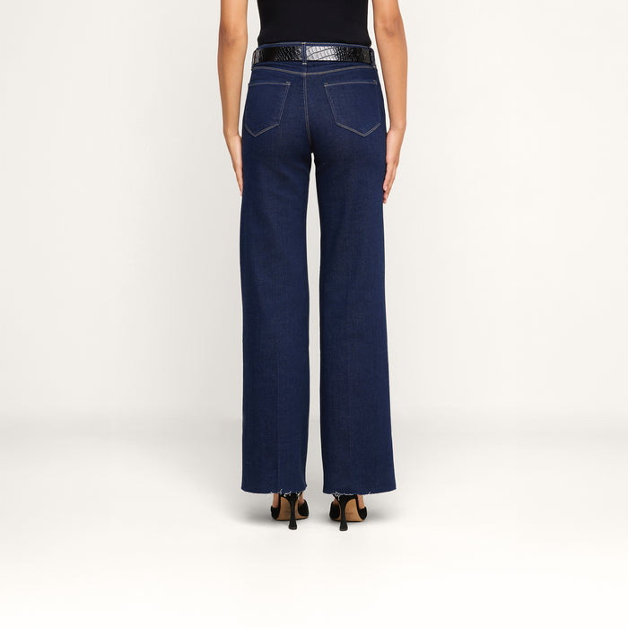 A person shown from the back against a plain white background is wearing the Scottie Wide-Leg Jean in dark blue, featuring a high-rise wide-leg silhouette crafted from premium stretch denim, styled with a black belt and black heeled shoes.