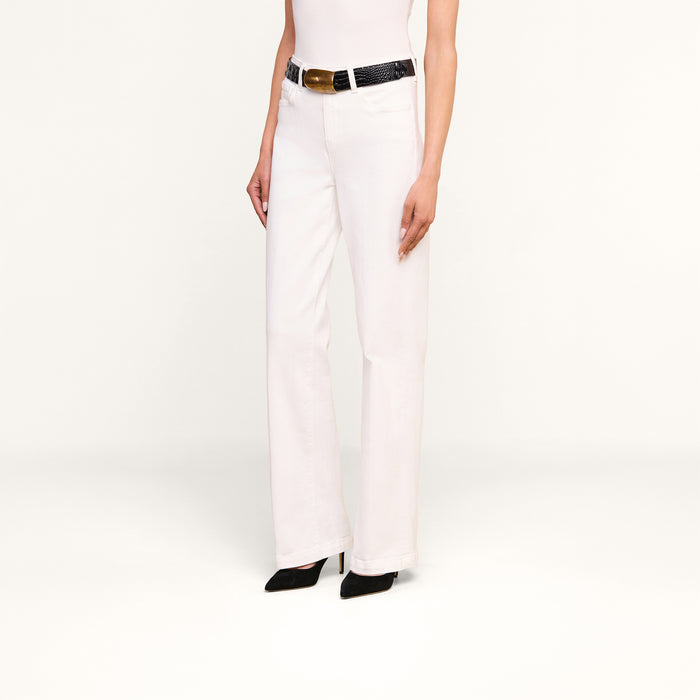 Person wearing the Scottie Wide-Leg Jean in white, featuring a high-rise waistband, styled with a black textured belt and black pointed-toe heels. The upper body is partially out of frame, and the background is plain white.