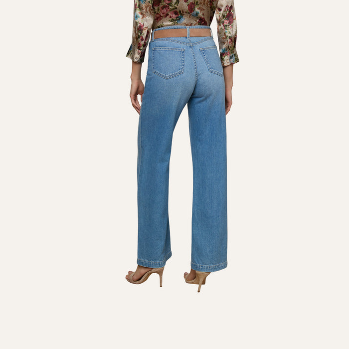 A woman is shown from the back against a plain background, wearing the Scottie Wide-Leg Jean in a light wash with a high-rise contoured waistband, paired with a floral long-sleeve blouse and beige heels.