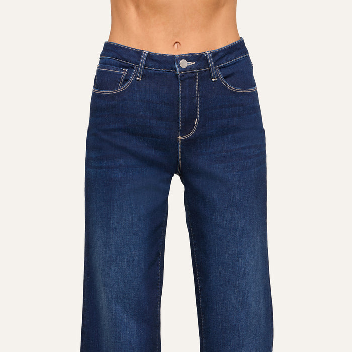 A person wearing high-waisted, dark blue jeans with white stitching is shown from waist to mid-thigh against a plain background.