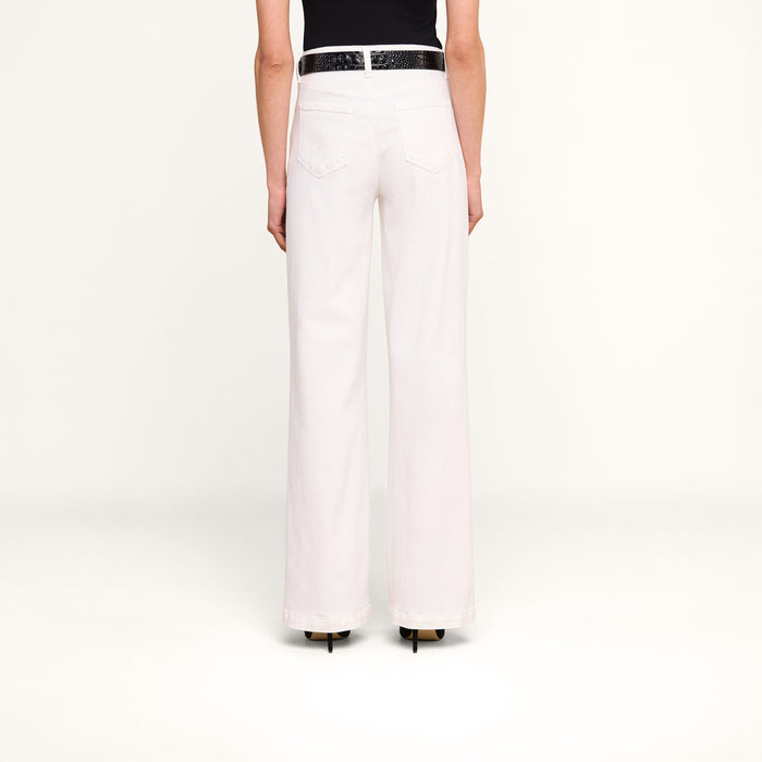 A person stands facing away from the camera, wearing the Scottie Wide-Leg Jean in white, featuring a high-rise waistband. The jeans are styled with a black belt and black top against a plain white background.