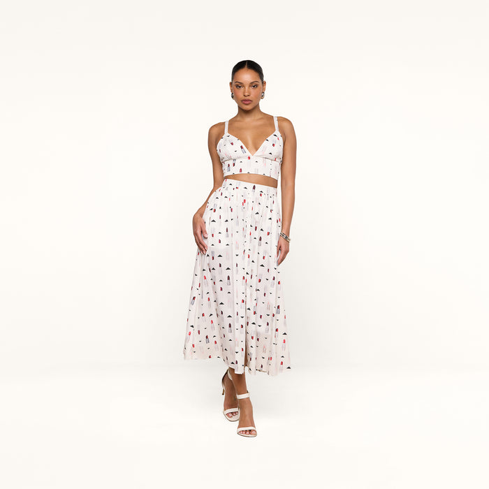 A woman wearing a white sleeveless crop top and the Seina Poplin Midi Skirt—a high-waisted, ankle-length skirt featuring a multicolored abstract print—stands against a plain white background.