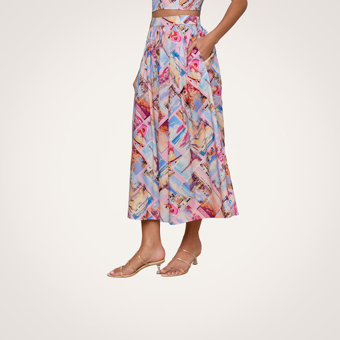 Woman wearing the Seina Poplin Midi Skirt—a colorful, patterned high-waisted pleated midi skirt with pockets—paired with a matching crop top and sandals, standing against a plain white background.