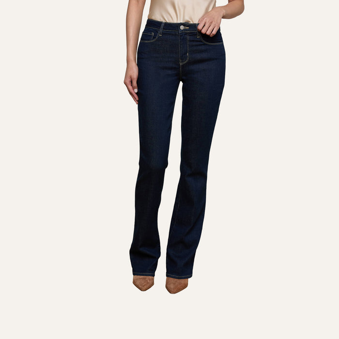 A person wearing the Selma Bootcut Jean in high-rise dark blue stretch denim and tan pointed-toe shoes stands against a plain light background, with their face not visible.