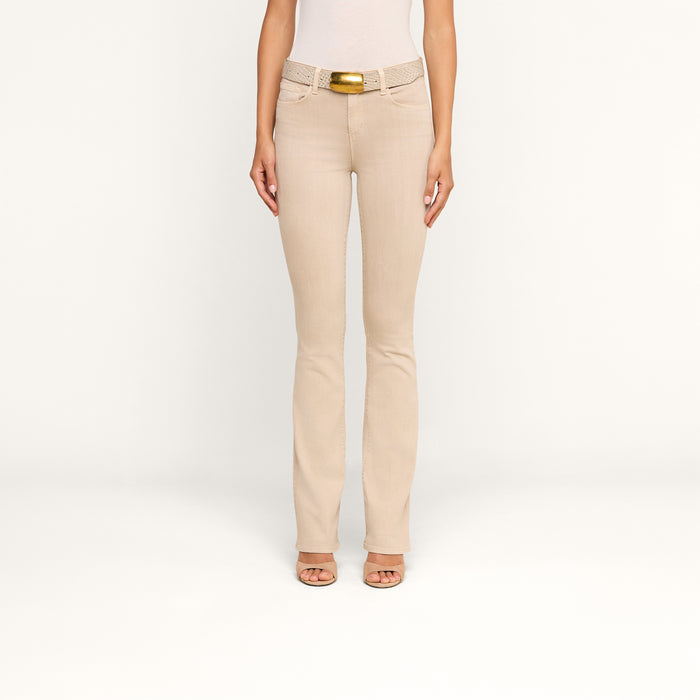 Wearing the Selma Bootcut Jean in beige stretch denim, styled with a matching beige belt featuring a gold buckle and open-toe heels, this person stands against a plain white background with only their lower body fully visible.