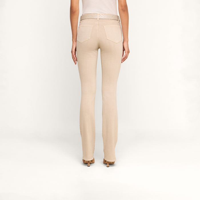 A person stands facing away, wearing the Selma Bootcut Jean in light beige stretch denim with a contoured waistband and high-heeled shoes, set against a plain white background.