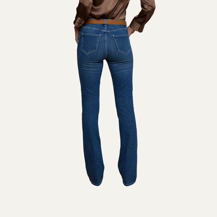 A person wearing the Selma Bootcut Jean in blue super stretch denim and a brown satin top is shown from the back, standing against a plain, light background.