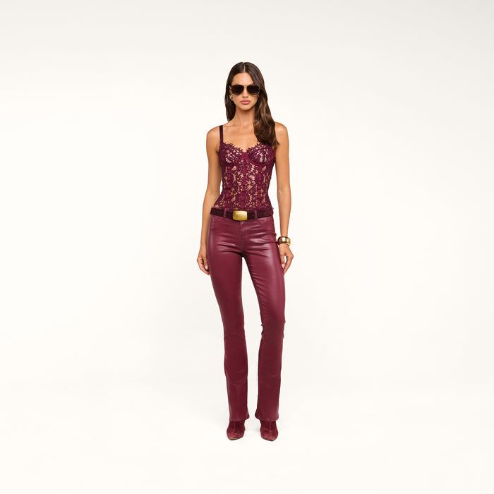 A woman wearing sunglasses, a burgundy lace top, and the Selma Coated Bootcut Jean stands against a plain white background.