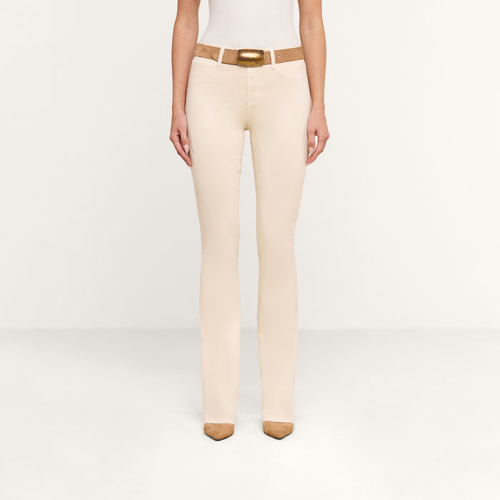 A person wearing the Selma Coated Bootcut Jean in beige, paired with a white top, a tan belt with a gold buckle, and tan pointed-toe shoes stands against a plain white background. Only the lower body is visible.