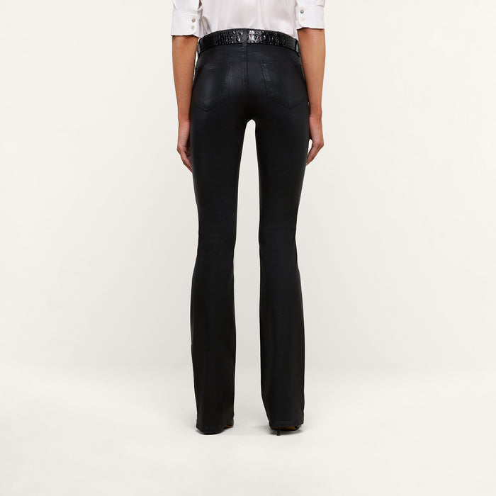 A person stands with their back to the camera, wearing a white shirt and the Selma Coated Bootcut Jean in black. The background is plain and light-colored.