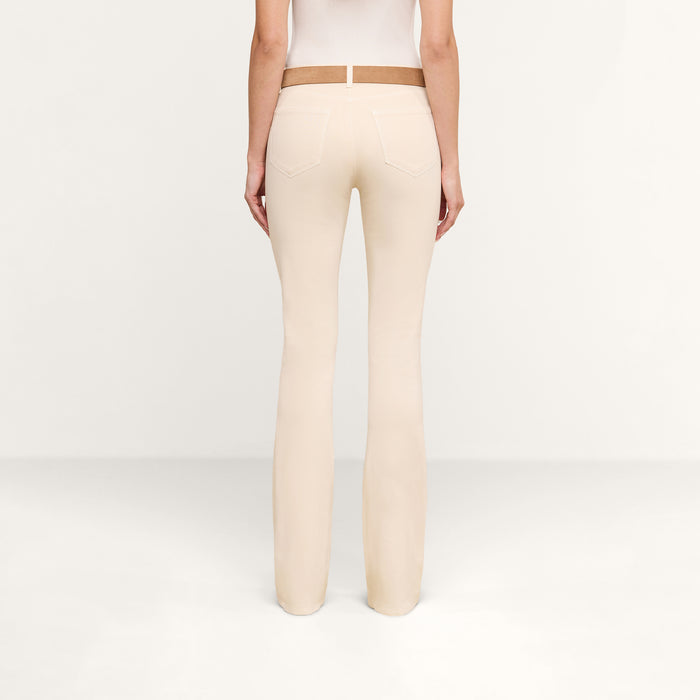 A person is shown from the back, standing in a plain, light-colored room, wearing the Selma Coated Bootcut Jean and a white top.
