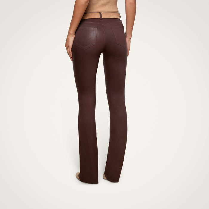A person is shown from the back, standing against a plain light background, wearing the Selma Coated Bootcut Jean in a high-waisted, chocolate brown style.