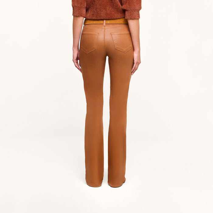 A person models the Selma Coated Bootcut Jean in a high-waisted, camel hue, paired with a dark java brown top, photographed from the back against a plain white background.
