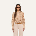 A woman wearing sunglasses and the Seychelle Cropped Eyelet Blouse stands facing forward against a plain light background, paired with cream pants and a brown belt.