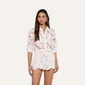 Woman wearing the Seychelle Cropped Eyelet Blouse and matching scalloped shorts, standing against a plain light background and looking slightly to the side with a neutral expression.