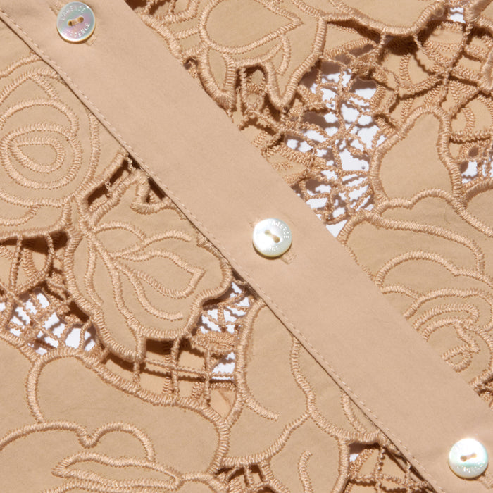 Close-up of the Seychelle Cropped Eyelet Blouse, showcasing beige floral lace fabric paired with a strip of solid beige poplin adorned with small, shiny buttons.