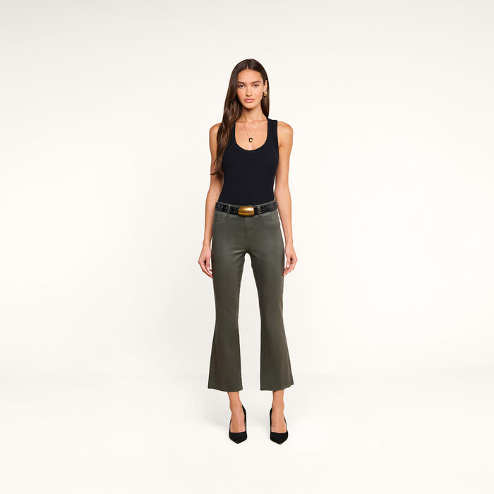 A woman stands facing forward against a plain white background, wearing the Shania Racerback Tank in black, olive green flared pants with a belt, black heels, and a necklace.