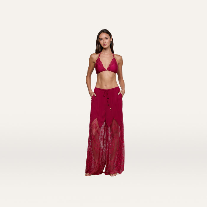 A woman stands against a plain white background wearing a red halter bralette and the Sharon Cover-Up Pant, which features sheer lace panels, pockets, and a drawstring waist.
