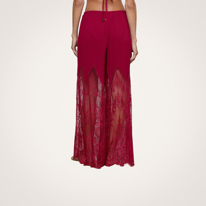 A person is shown from the back against a plain light background, wearing the Sharon Cover-Up Pant—high-waisted, wide-leg pants in red lace featuring sheer lace panels, a solid waistband, and a pleated upper section.