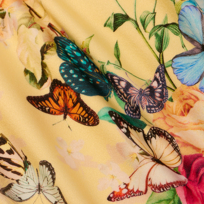 The Shiva One-Piece Swimsuit is crafted from smooth, yellow fabric adorned with colorful butterflies in a variety of patterns, surrounded by green leaves and soft pastel flowers.