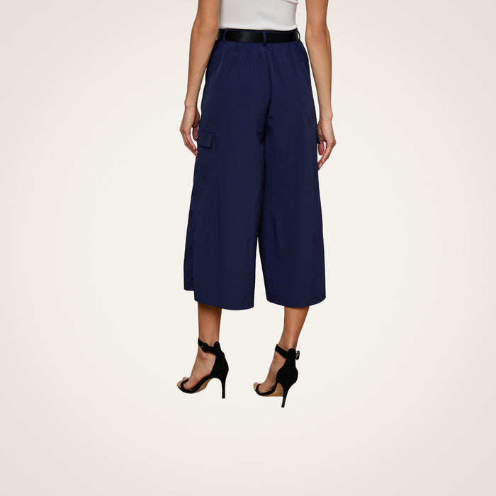 A person is shown from the back against a plain light background, wearing the Shoda Cropped Wide-Leg Pant in navy blue, paired with a white top and black high-heeled sandals.