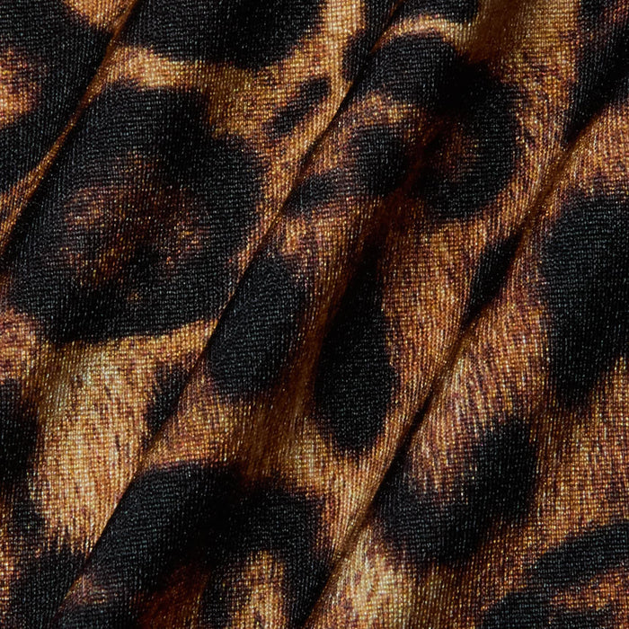 Close-up of fabric with a leopard print pattern, featuring black and brown spots on a tan background. The material, used for the Sirena Halter Bikini Top, displays visible folds and texture—perfect for bold swimwear style.