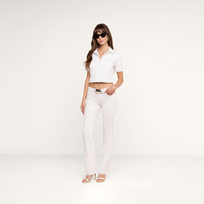 A woman wearing sunglasses, a short-sleeved cropped white top, the Sneeki Low-Rise Straight-Leg Jean in super stretch denim with a raw hem, and heeled sandals stands against a plain white background.