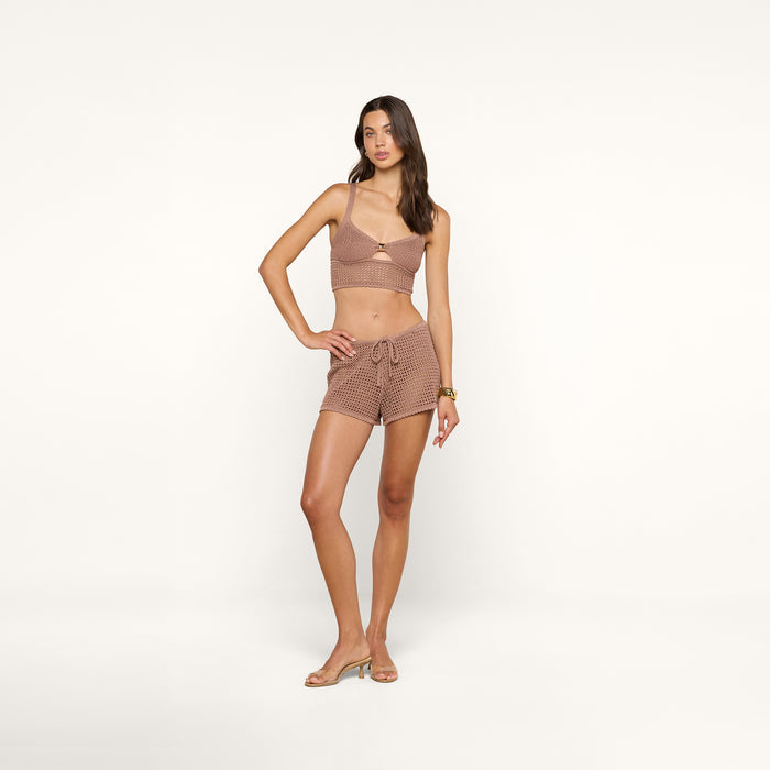 A woman stands against a plain white background wearing a brown checkered crop top and the Solan Pointelle Knit Short with sandals. She has one hand on her hip and looks confidently at the camera.