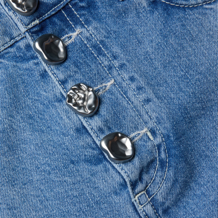 Close-up of the Solene Jean Mini Skirt in a light wash, crafted from all-cotton denim and featuring unique, irregular silver metal buttons sewn along a seam to highlight the stitching details and textured fabric.