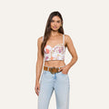 A woman wearing the Sonya Bustier in a baroque toile print paired with light blue jeans stands with one hand in her pocket and the other resting on her belt, smiling at the camera.
