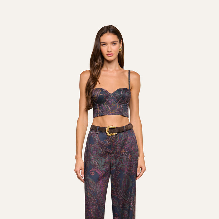 A woman with long brown hair wears the Sonya Bustier in navy paisley, paired with matching high-waisted pants and a wide brown belt, standing against a plain off-white background.