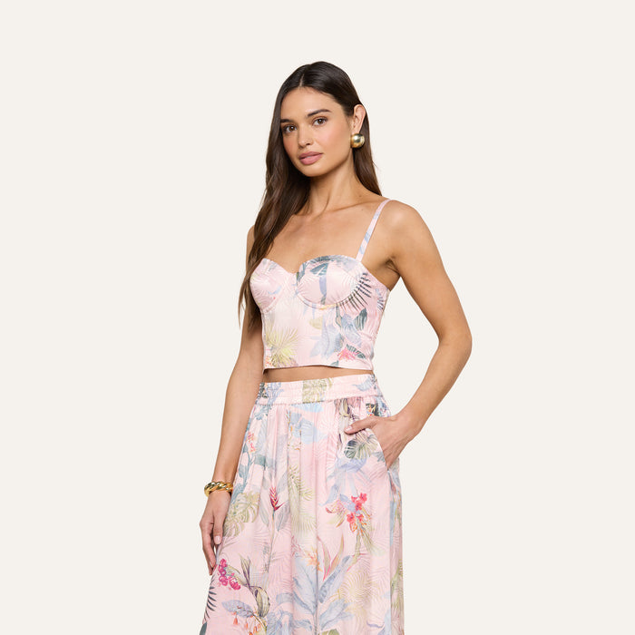 A woman wearing the Sonya Bustier, a light pink floral-patterned bustier top, paired with a matching skirt, poses with one hand in her pocket against a plain background.