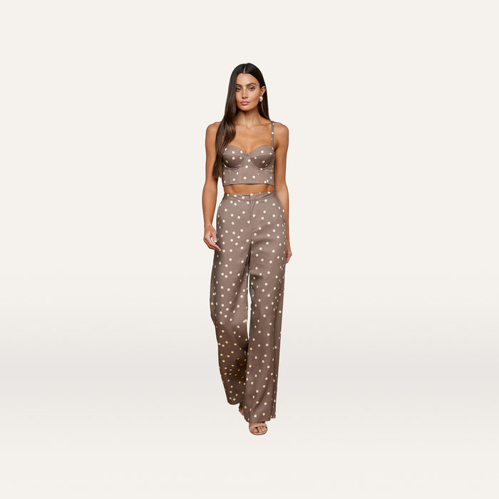 A woman walks forward against a plain white background wearing the Sonya Bustier, a cardamom polka dot crop top with a smocked back, paired with matching high-waisted wide-leg pants crafted from lightweight twill.