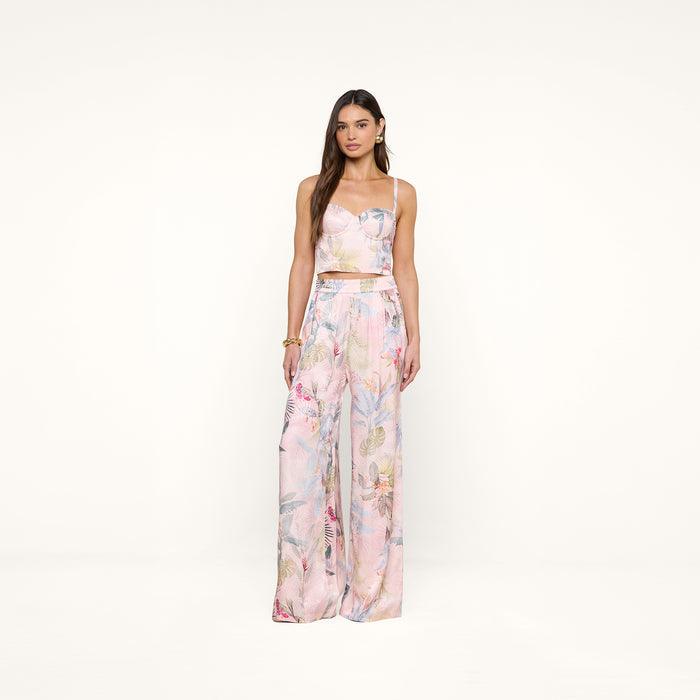 A woman stands against a plain background wearing the Sonya Bustier—a pastel floral top—paired with matching wide-leg pants in lightweight twill, her long hair down and minimal accessories completing the look.