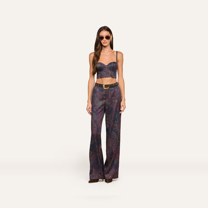 A woman wearing sunglasses and the Sonya Bustier—a navy paisley top with built-in support—paired with matching high-waisted, wide-leg pants featuring a belt. She stands facing forward against a plain light background.