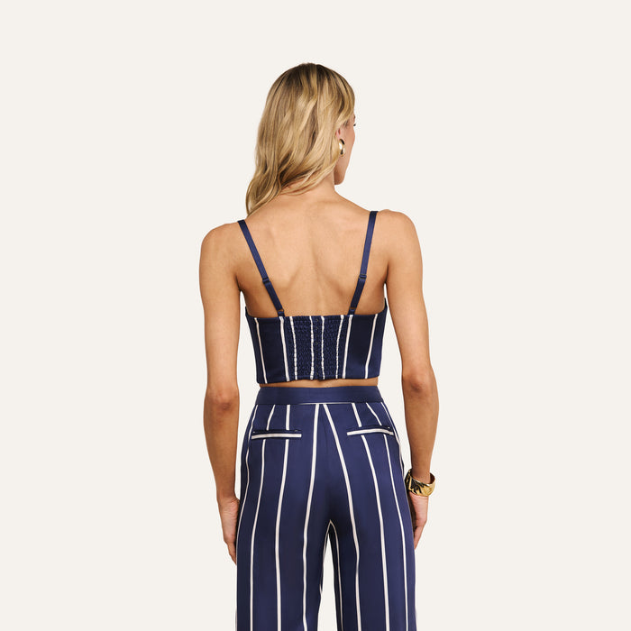 A woman with long blonde hair, seen from the back, wears the Sonya Bustier and matching high-waisted pants featuring navy fabric with white vertical stripes.