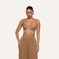A woman wearing the Sonya Linen-Blend Bustier with high-waisted, loose tan pants stands against a plain, light background. She accessorizes with gold hoop earrings and a gold bracelet, and her hair is tied back.